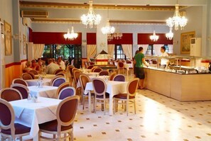 A dining area with multiple tables and chairs, a central counter, and chandeliers. - Zante Imperial Beach Hotel (Zakynthos)