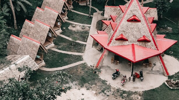 Un resort con cabañas de techo de paja dispuestas en forma de semicírculo, rodeado de densas palmeras.