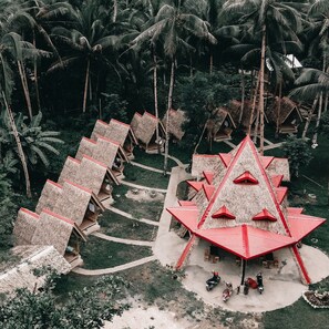 Un resort con cabañas de techo de paja dispuestas en forma de semicírculo, rodeado de densas palmeras.