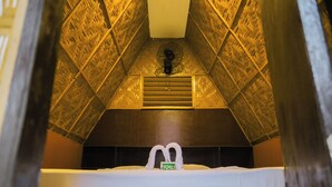 Habitación de hotel con un diseño geométrico único en el techo, una cama con el rótulo 'TOILET' y un ventilador en el centro.