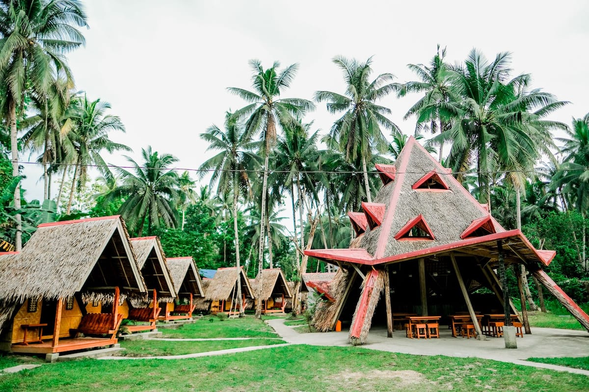 Thatched-roof huts with a central open area, surrounded by palm trees.