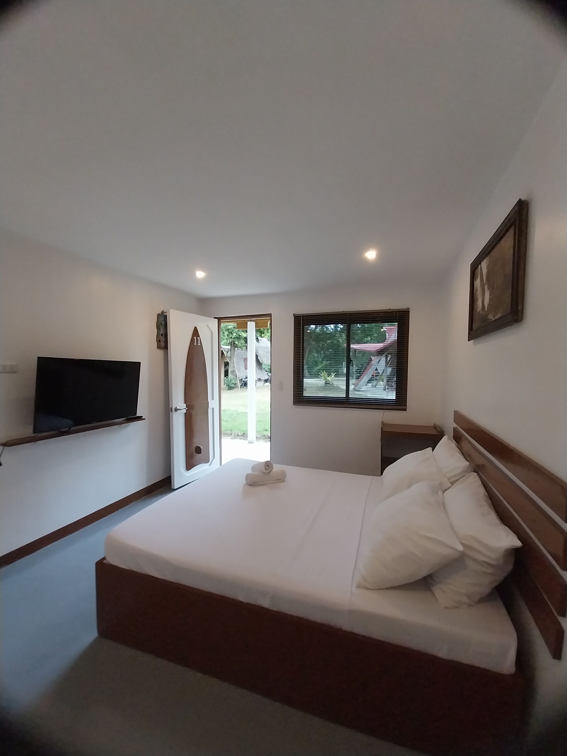 Un dormitorio con cama, televisión, ventana y puerta que da al exterior.