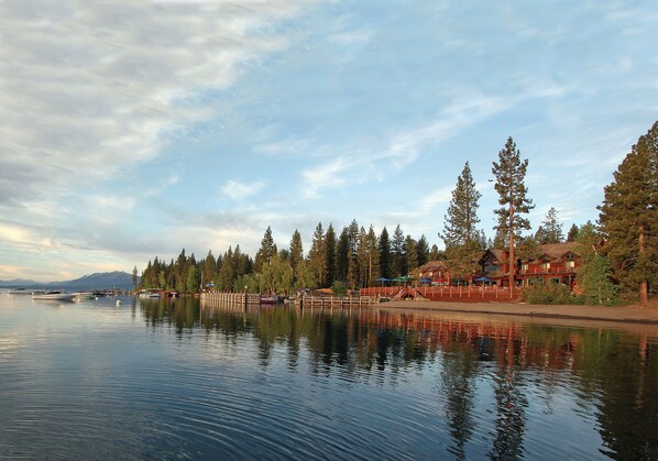 A lakeside view with a wooden dock, boats, and a cabin-style building with a thatched roof. - Sunnyside Restaurant & Lodge (Tahoe City)