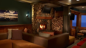 A cozy living room with a stone fireplace, comfortable seating, and a television mounted on the wall. - Sunnyside Restaurant & Lodge (Tahoe City)