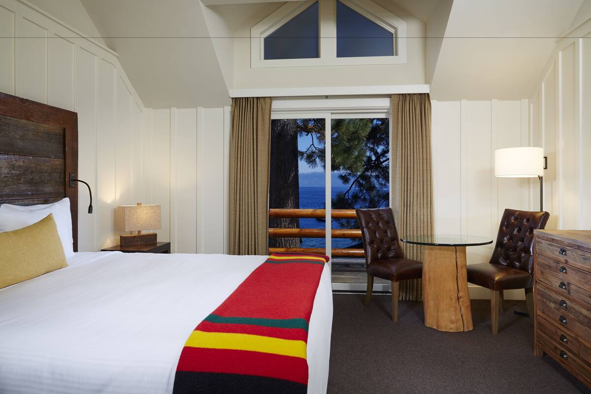 Ein Hotelzimmer mit einem großen Bett, einem Holzschrank, einem kleinen Tisch und Blick ins Freie.