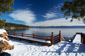 A wooden dock extending into a calm lake with snow on the ground and mountains in the background.