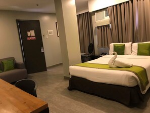 Quarto de hotel com cama, escrivaninha, cadeira, sofá e porta com placa de 'Não Fumar'.