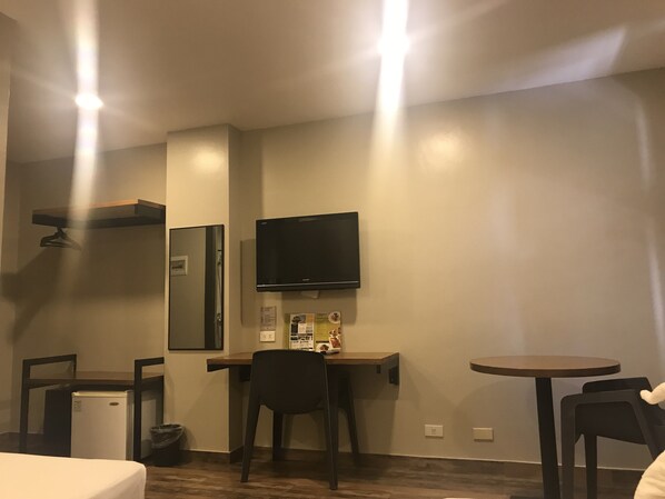 A compact hotel room with a desk, a chair, a small table, a TV mounted on the wall, a mini-fridge, and a trash bin. - Cebu R Hotel - Capitol (Cebu City)