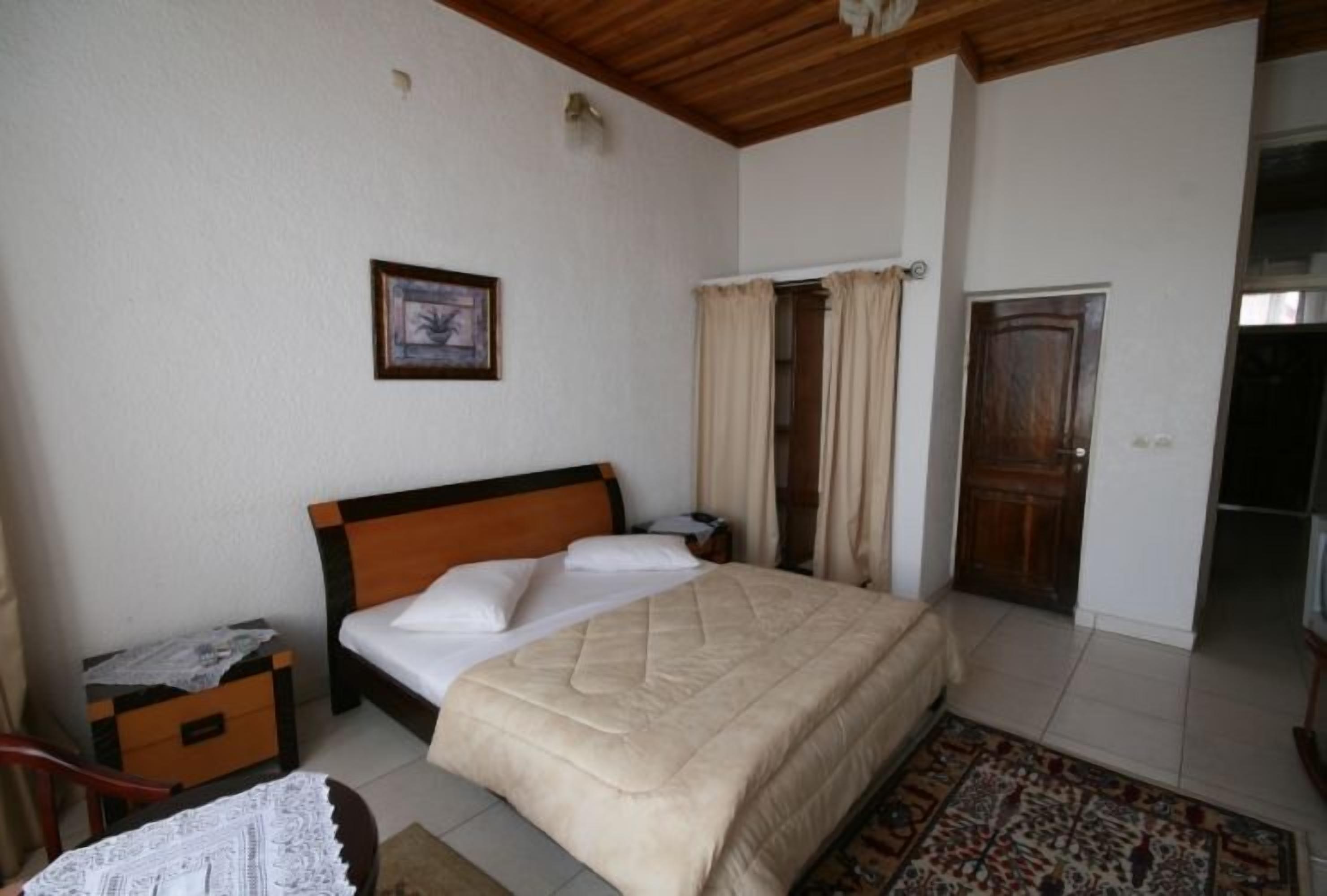 A bedroom with a bed, a nightstand, a chair, a door, and a window with curtains.