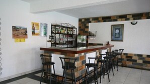 Een bar met een toonbank, krukken en een plank met flessen.