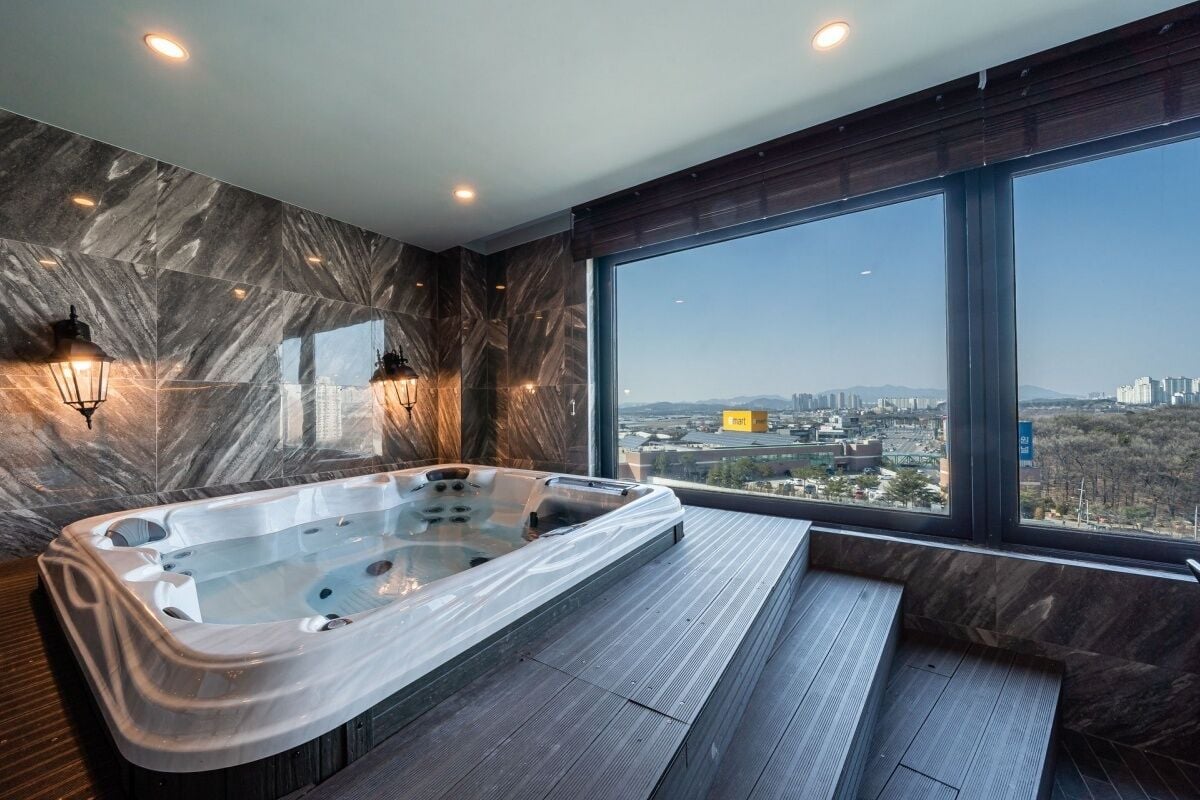 A modern bathroom with a large bathtub, marble walls, and a city view.