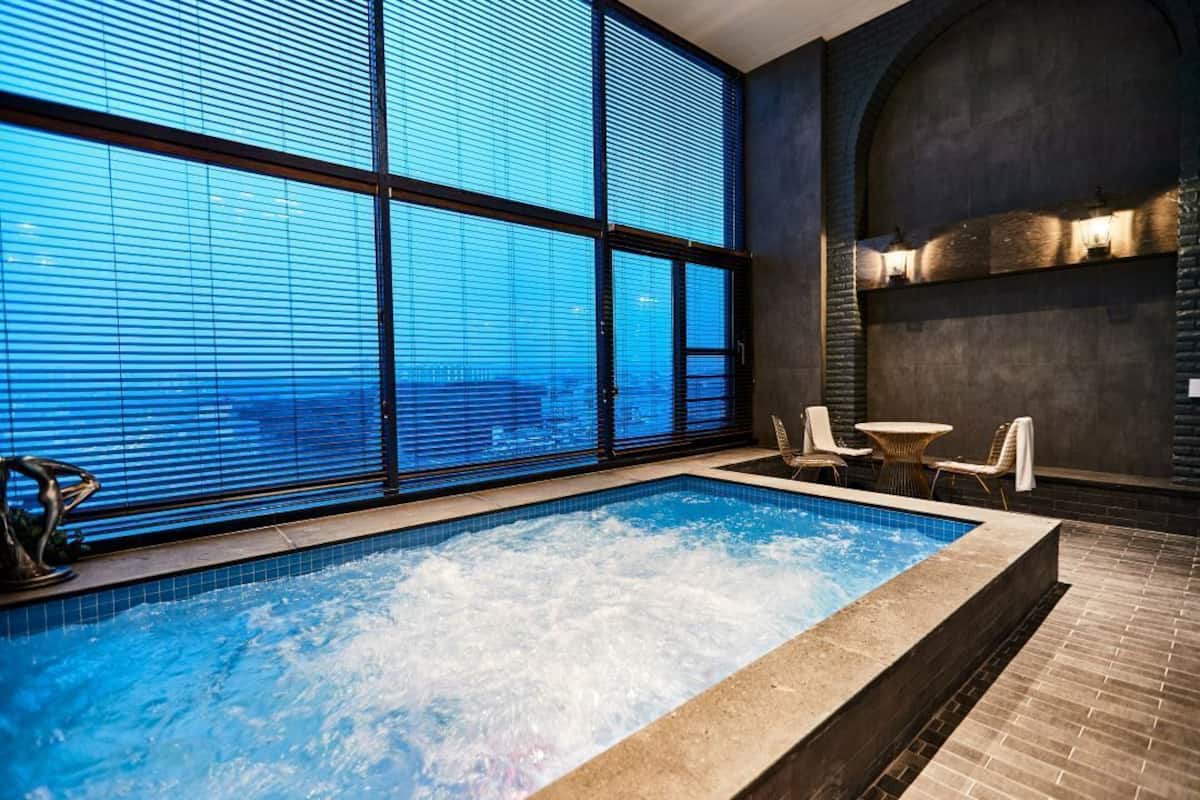 A spa area with a hot tub, large windows, and a brick wall.