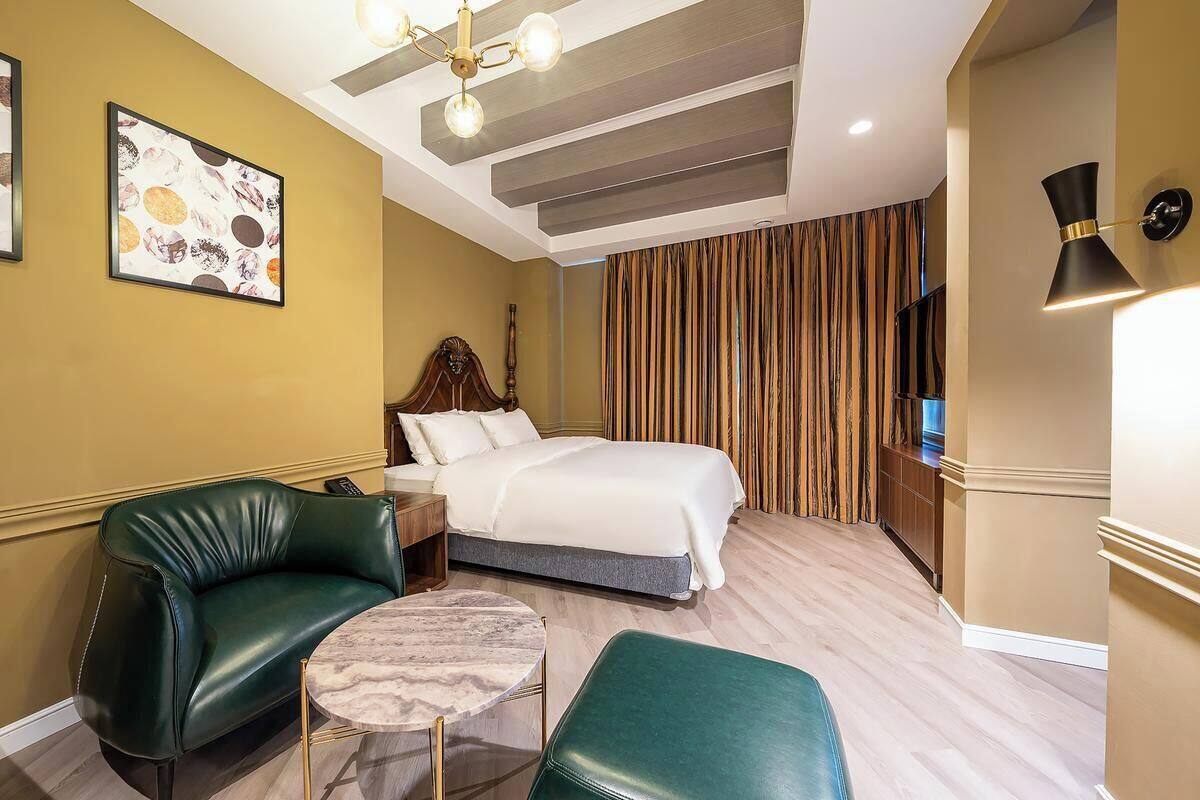 A hotel room with a bed, a green leather sofa, a small round table, and a TV on the wall.