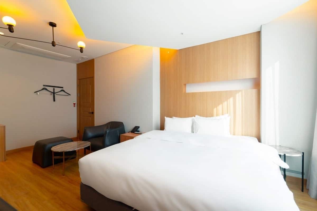 A hotel room with a large bed, a small table, a chair, and a coat rack.