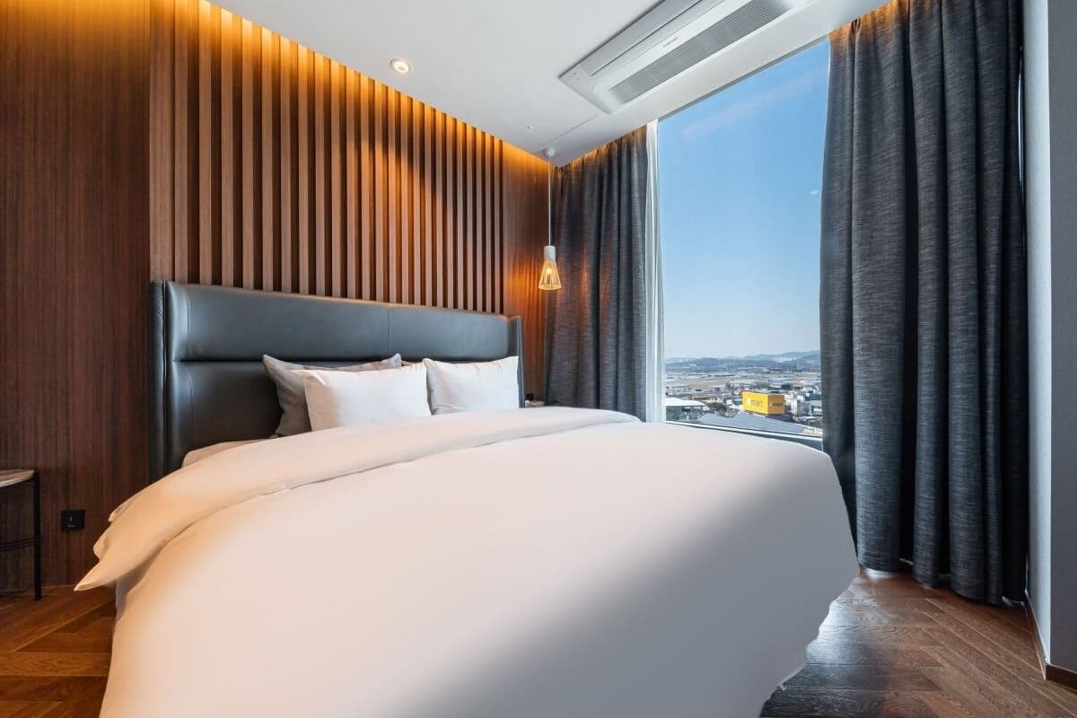 A modern hotel room with a large bed, a city view, and a wooden panel wall.