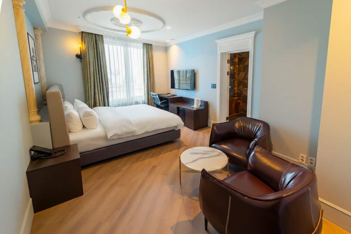 A hotel room with a bed, a desk, a leather chair, a TV, and a small table.