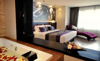 A modern hotel room with a large bed, a sitting area, and a bathtub with rose petals.