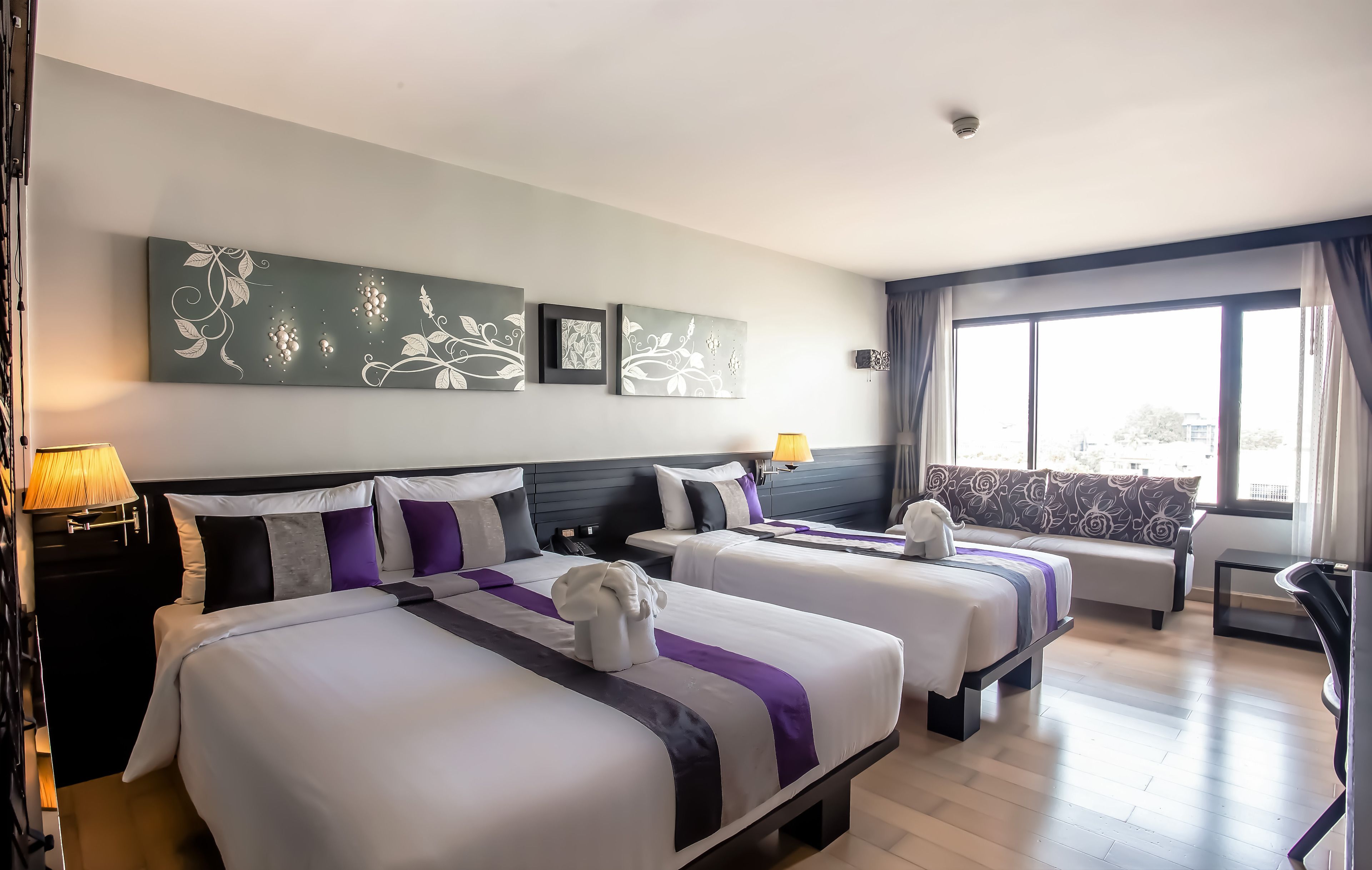 A hotel room with two beds, a sofa, a desk, and a large window.