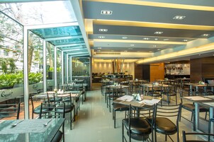 A modern restaurant with glass walls, multiple dining areas, and a kitchen in the background.