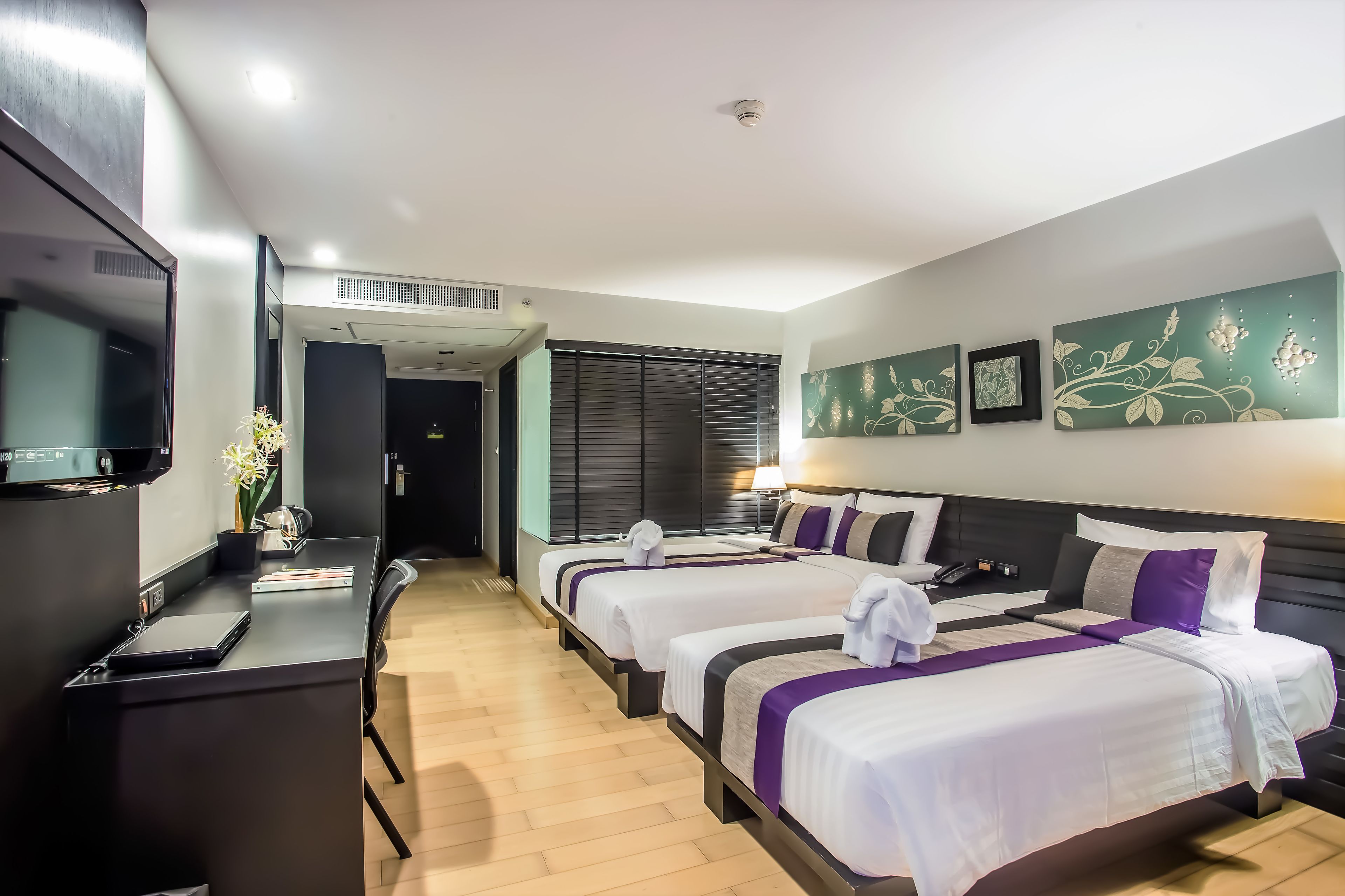 A hotel room with two beds, a desk, a TV, and artwork on the wall.