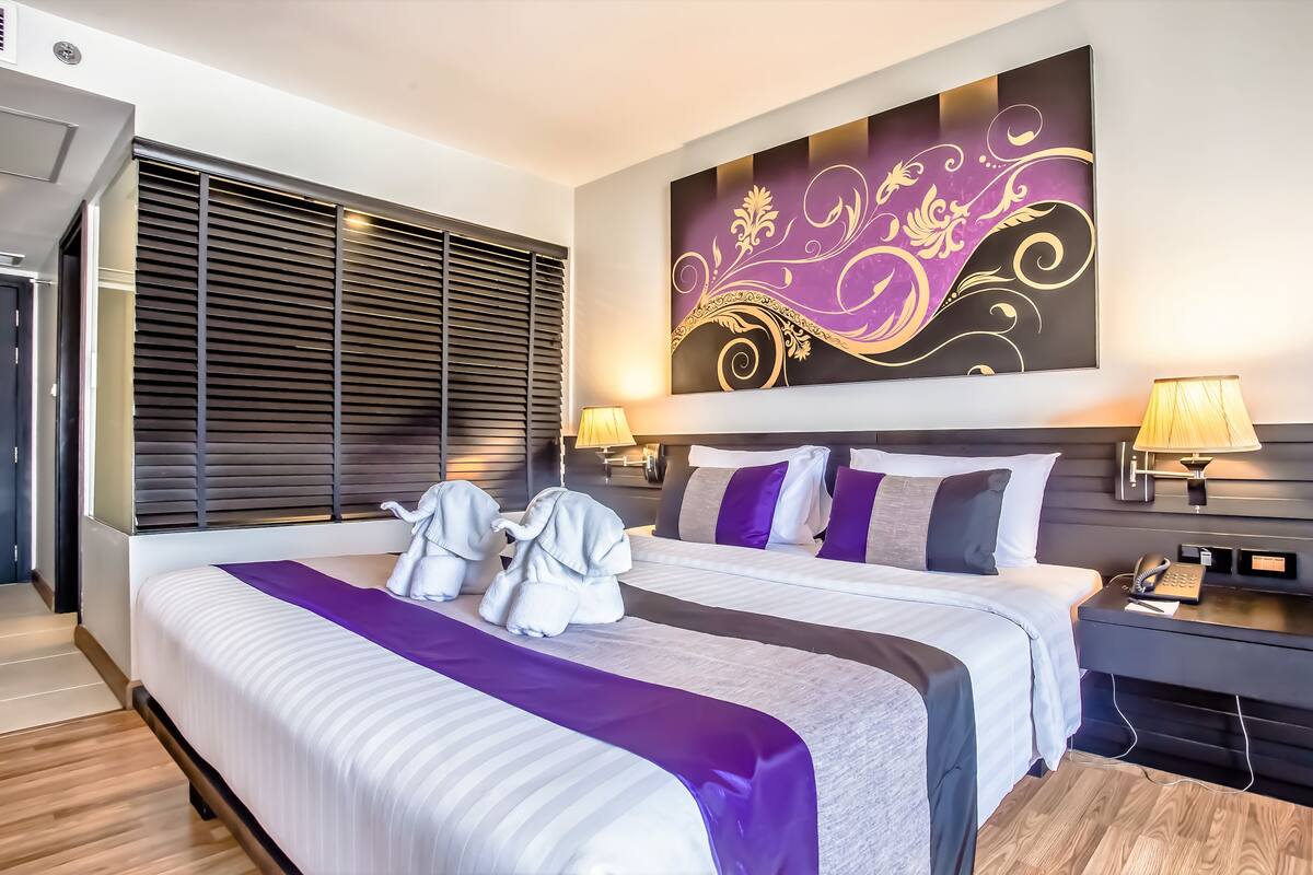 Een moderne hotelkamer met een groot bed, twee bedlampen, een tv aan de muur en een raam met zonwering.