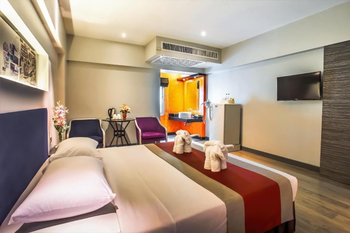 A hotel room with a bed, a desk, a chair, a TV, and a bathroom visible through an open door.