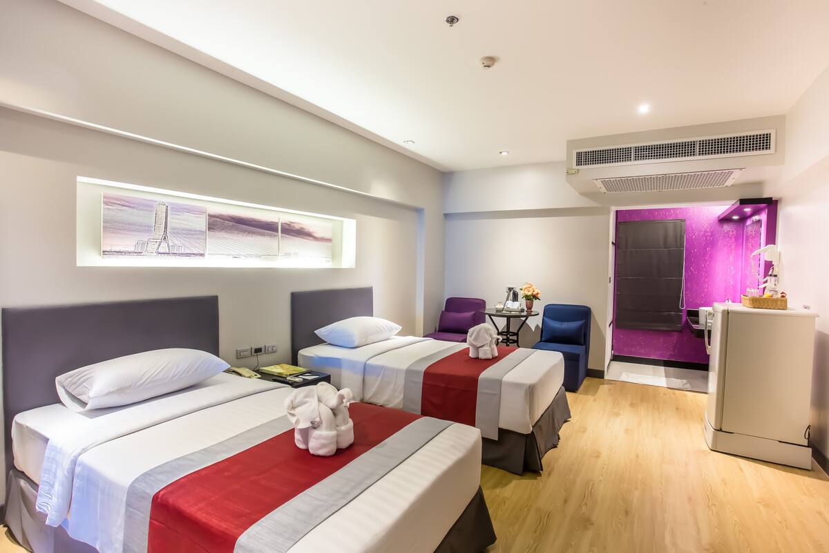 Een hotelkamer met twee bedden, een bureau, een stoel, een koelkast en een paarse wand.