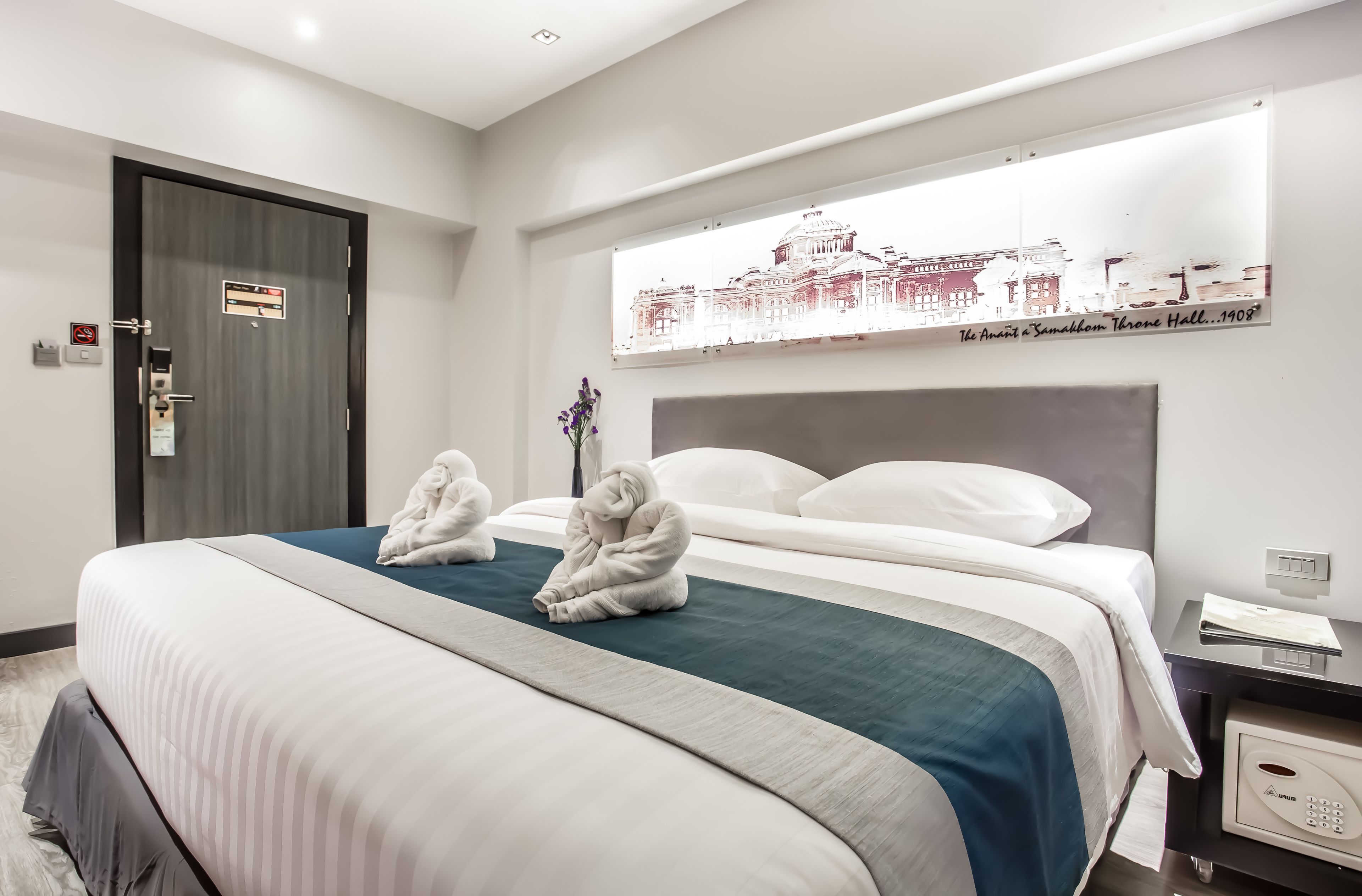 A hotel room with a large bed, a headboard, a nightstand, and a wall-mounted artwork.
