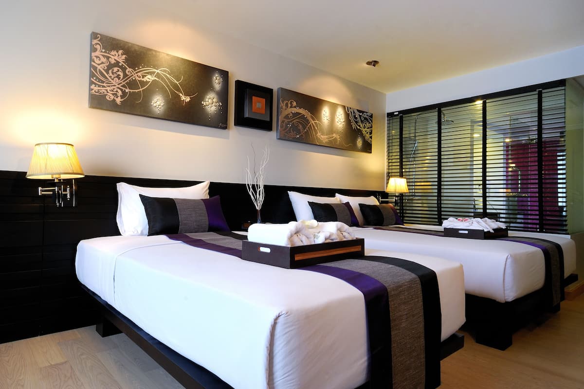 Een hotelkamer met twee bedden, een donker hoofdbord, een kunstwerk aan de muur en een raam met jaloezieën.