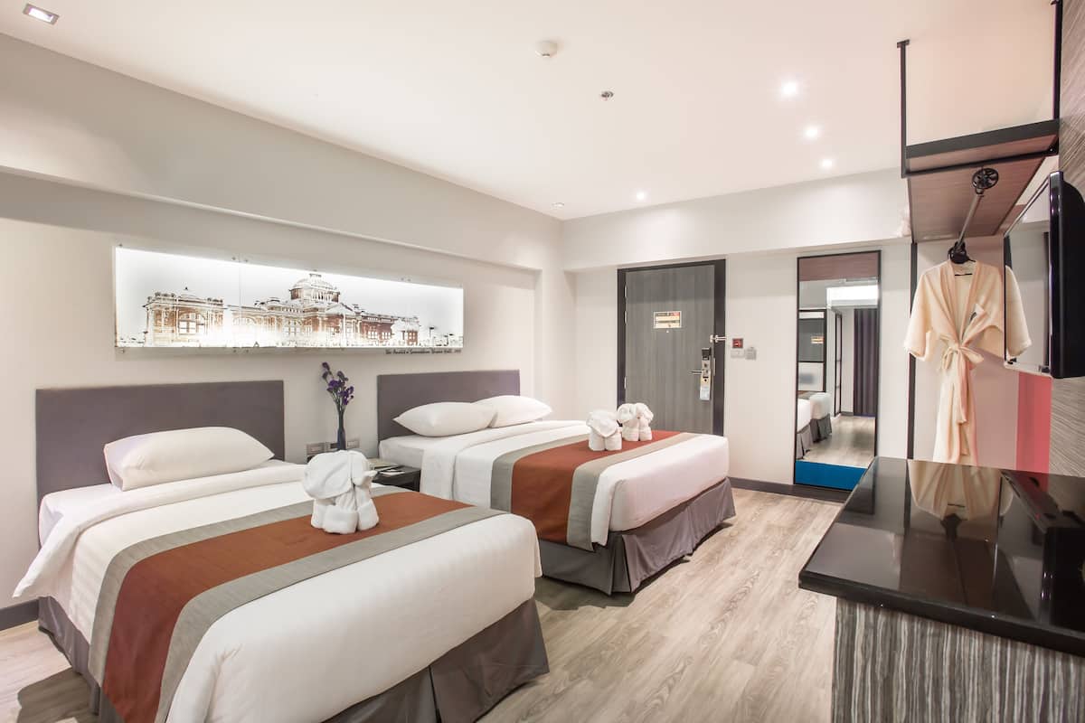 Een hotelkamer met twee bedden, een bureau, een spiegel en een ingelijst schilderij aan de muur.