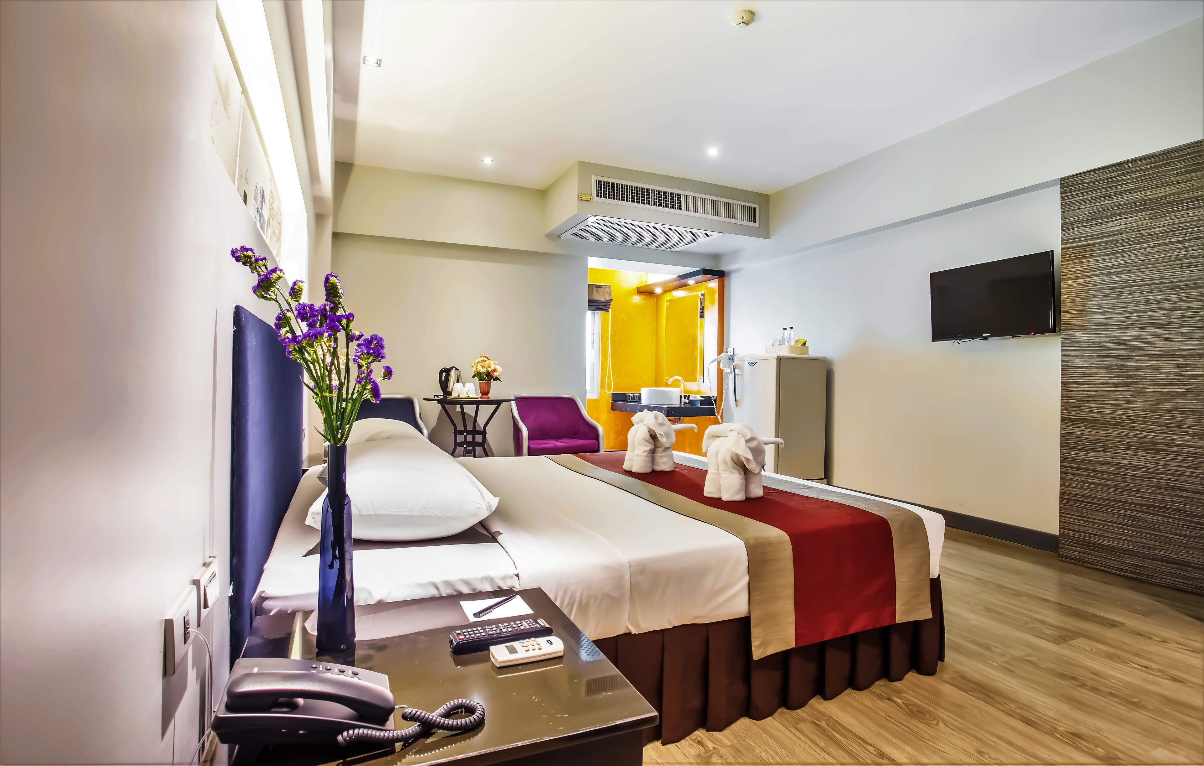 A hotel room with a bed, bedside table, phone, and a vase with flowers.