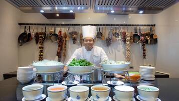 A chef in a modern kitchen with various cooking utensils hanging on the wall, a buffet table with bowls and plates, and a clean, organized layout.