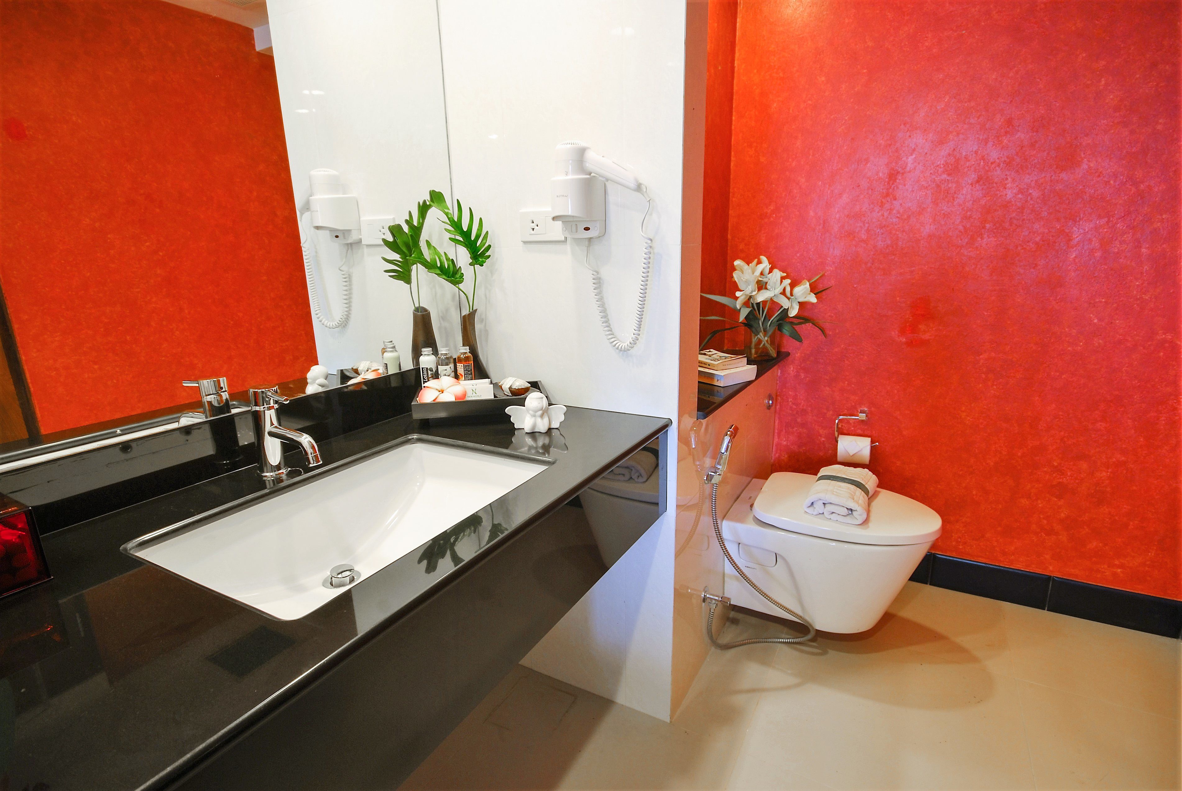 Un bagno moderno con lavandino nero, water bianco e pareti rosse.
