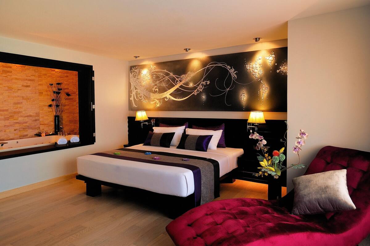 Een moderne slaapkamer met een houten accentmuur, een groot bed met meerdere kussens, een rode fauteuil en een decoratief wandobject.