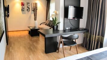 A modern hotel room with a flat-screen TV mounted on the wall, a wooden floor, a dining area with a table and chairs, and a large window with curtains.
