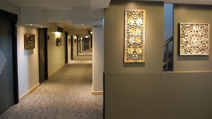 Pasillo de hotel con suelo alfombrado, obras de arte enmarcadas en las paredes y una escalera a la derecha.