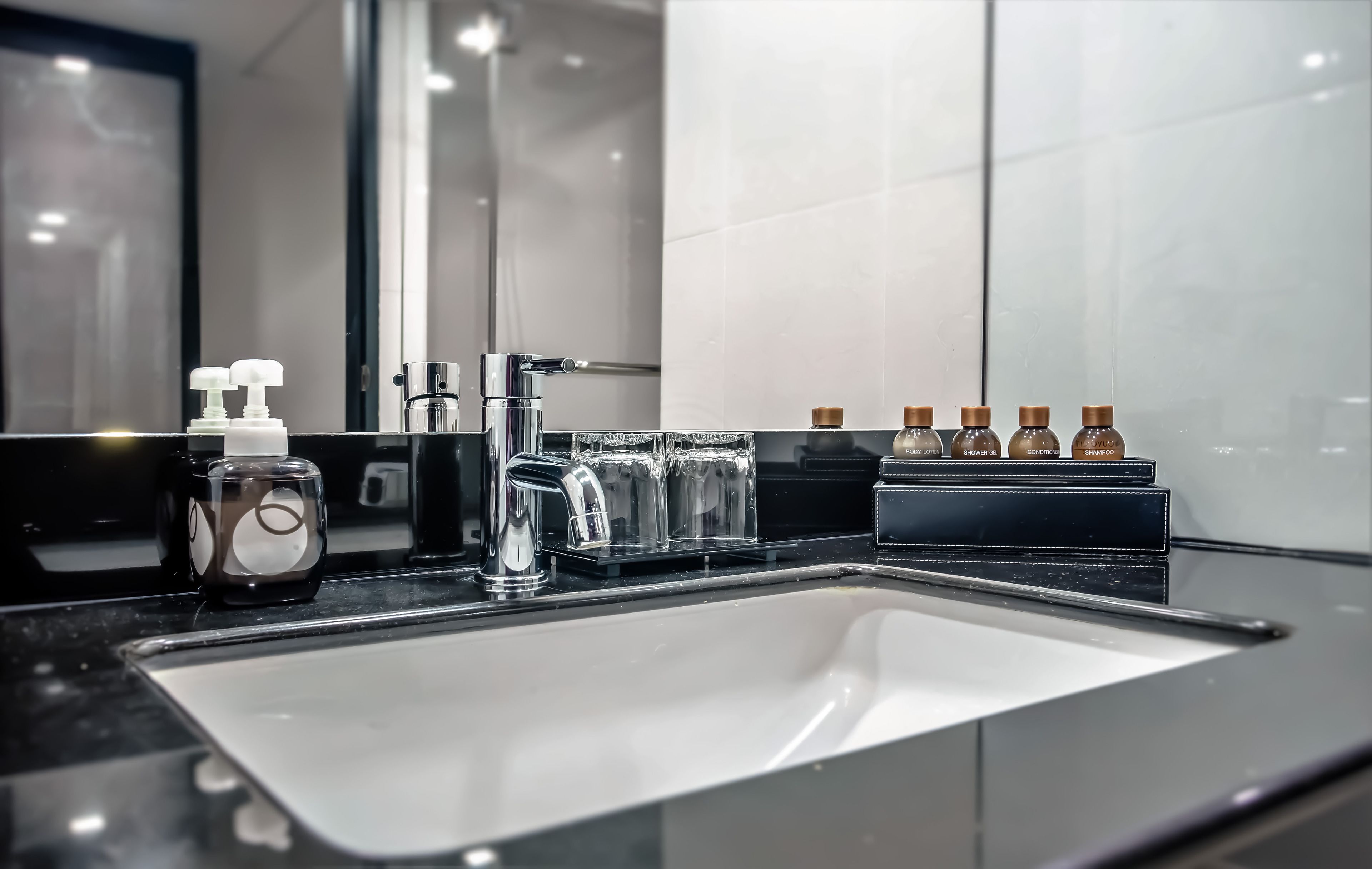 Une salle de bain moderne avec un grand miroir, un robinet chromé et un distributeur de savon en verre.