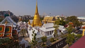 A traditional temple complex with a prominent golden spire, surrounded by white buildings with tiled roofs, and a water canal in the foreground.