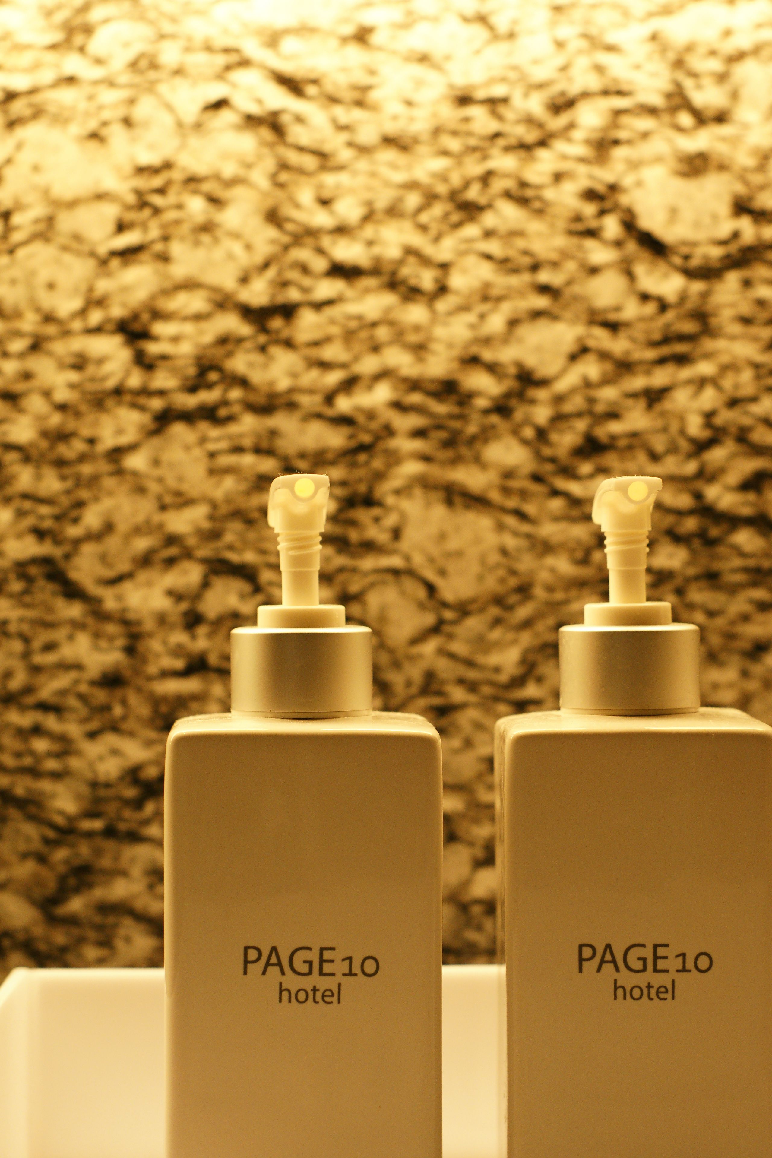 Two white bottles with pumps labeled "PAGE10 hotel" against a textured wall.