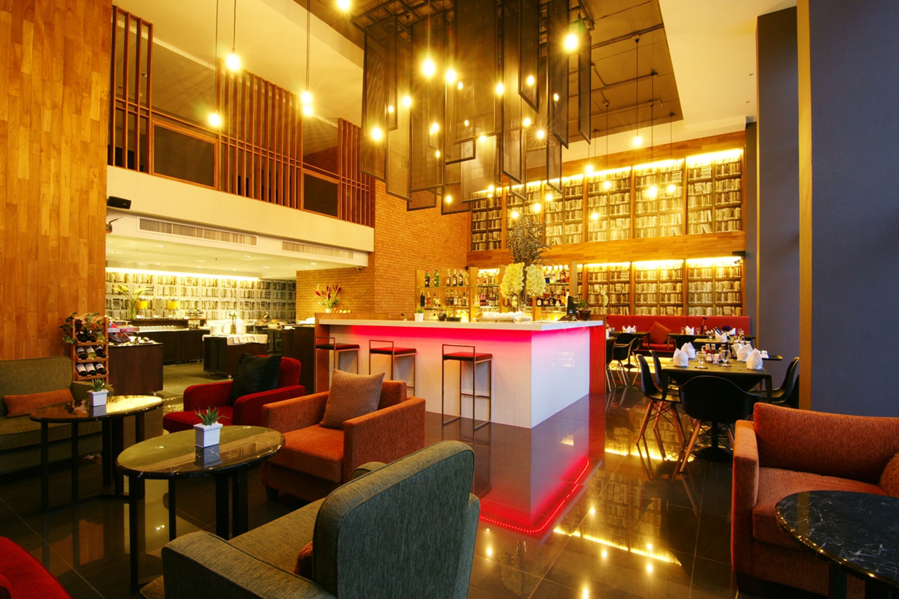 A modern hotel lobby with a bar area, seating arrangements, and a large bookshelf.