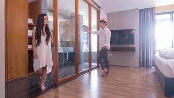 Habitación de hotel moderna con puerta corredera de cristal que da a un baño, un televisor de pantalla plana en la pared y suelo de madera.