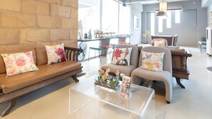 A modern living area with a stone wall, a sofa with floral cushions, a coffee table with a vase, and a view of the outside through large windows. - Plai And Herbs Suvarnabhumi Airport (Bang Phli)
