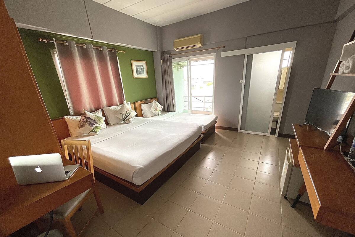 Ein Hotelzimmer mit einem großen Bett, einem Schreibtisch mit einem Laptop, einem Fernseher und einem durchgegangene Tür sichtbaren Badezimmer.
