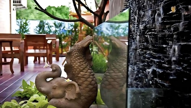 A decorative garden with a koi pond, a stone wall, and wooden furniture. - Plai And Herbs Suvarnabhumi Airport (Bang Phli)