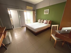 A bedroom with a bed, a desk with a laptop, a chair, and a door leading to a balcony. - Plai And Herbs Suvarnabhumi Airport (Bang Phli)