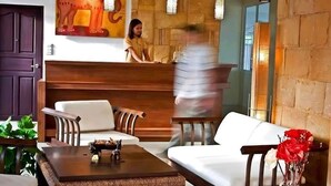 A reception area with a receptionist, a reception desk, a sofa, a coffee table, and a vase with flowers. - Plai And Herbs Suvarnabhumi Airport (Bang Phli)