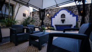 Un patio al aire libre con mobiliario de mimbre, una pared de piedra con detalles azules y una pared con arco azulado de azulejos.