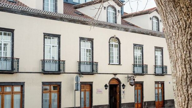 Un edificio con varias puertas y ventanas de madera, un cartel que indica un hotel y una calle adoquinada.