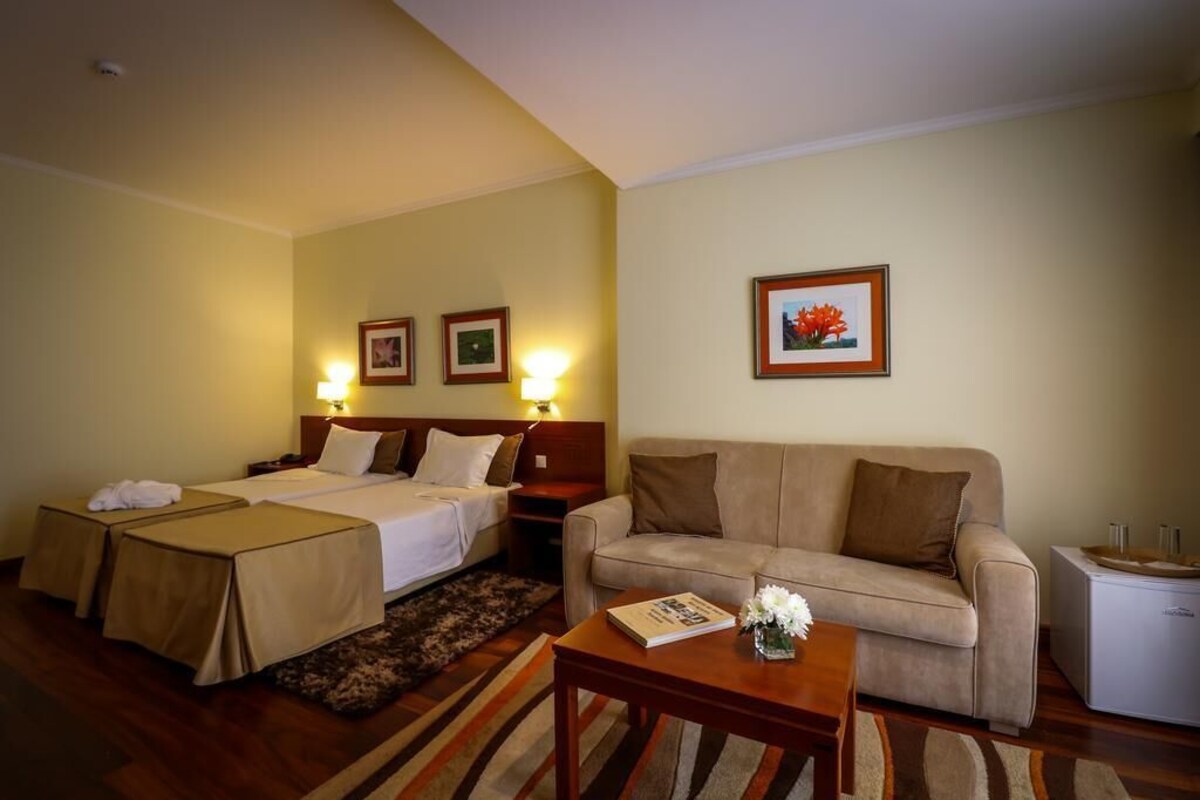 A hotel room with two beds, a sofa, a small table, and a refrigerator.