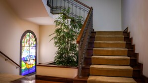 Una escalera de madera con barandilla, un vitral y una planta en maceta.